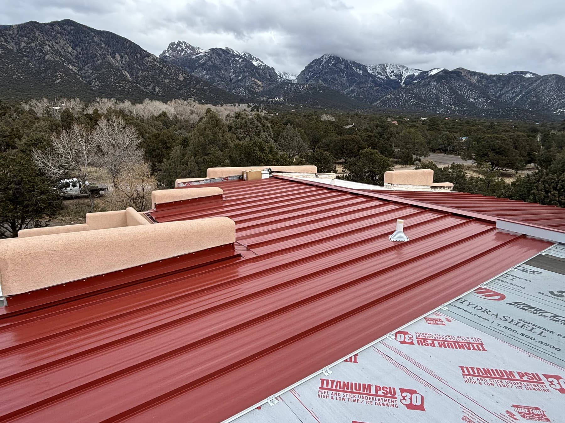 Barn-red standing-seam roofing during installation in Crestone, with mountains beyond